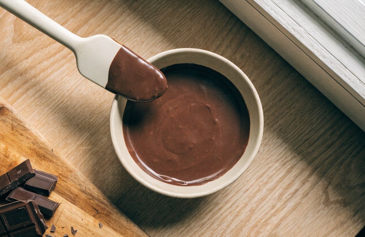 Small bowl of smooth, glossy melted dark chocolate with chopped chocolate pieces nearby