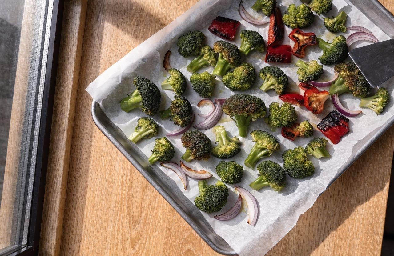 Roasted broccoli, red bell pepper and red onion with charred edges on a parchment-lined sheet