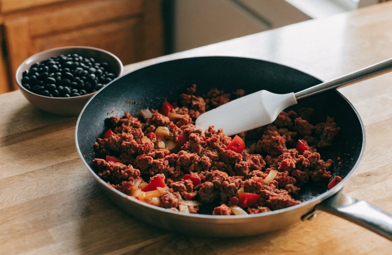 Crumbled ground turkey with diced red pepper and onion browning in a nonstick skillet