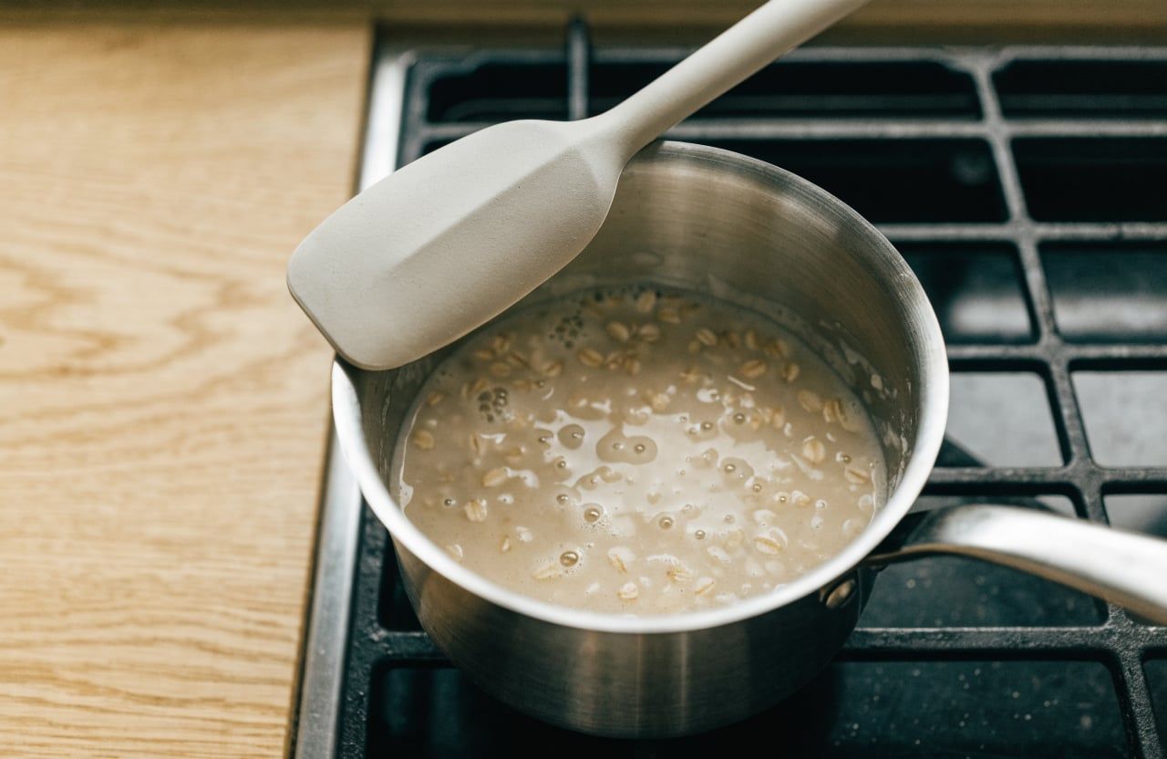 Creamy rolled oats simmering in milk in a small saucepan with a spatula