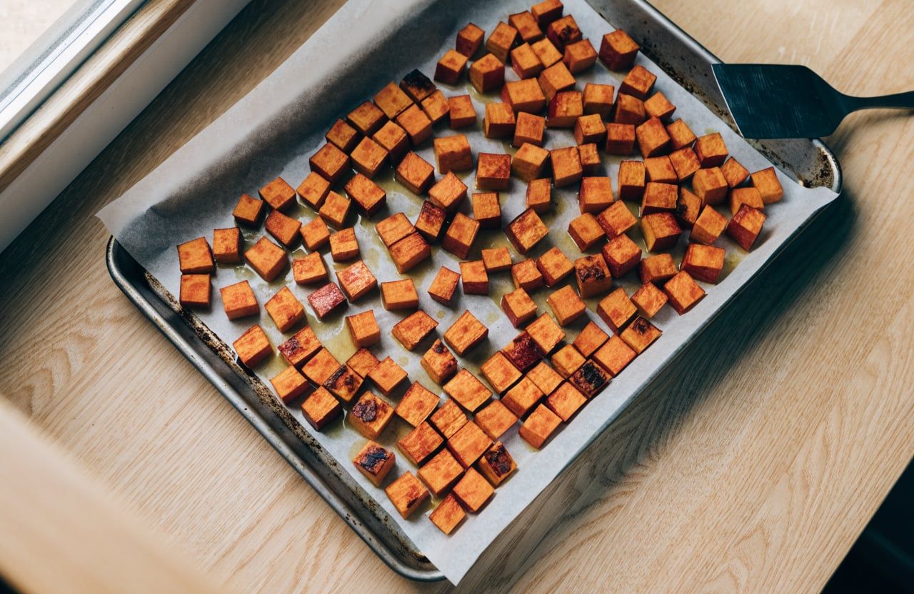 Roasted sweet potato cubes with caramelized edges spread out on a parchment-lined baking sheet