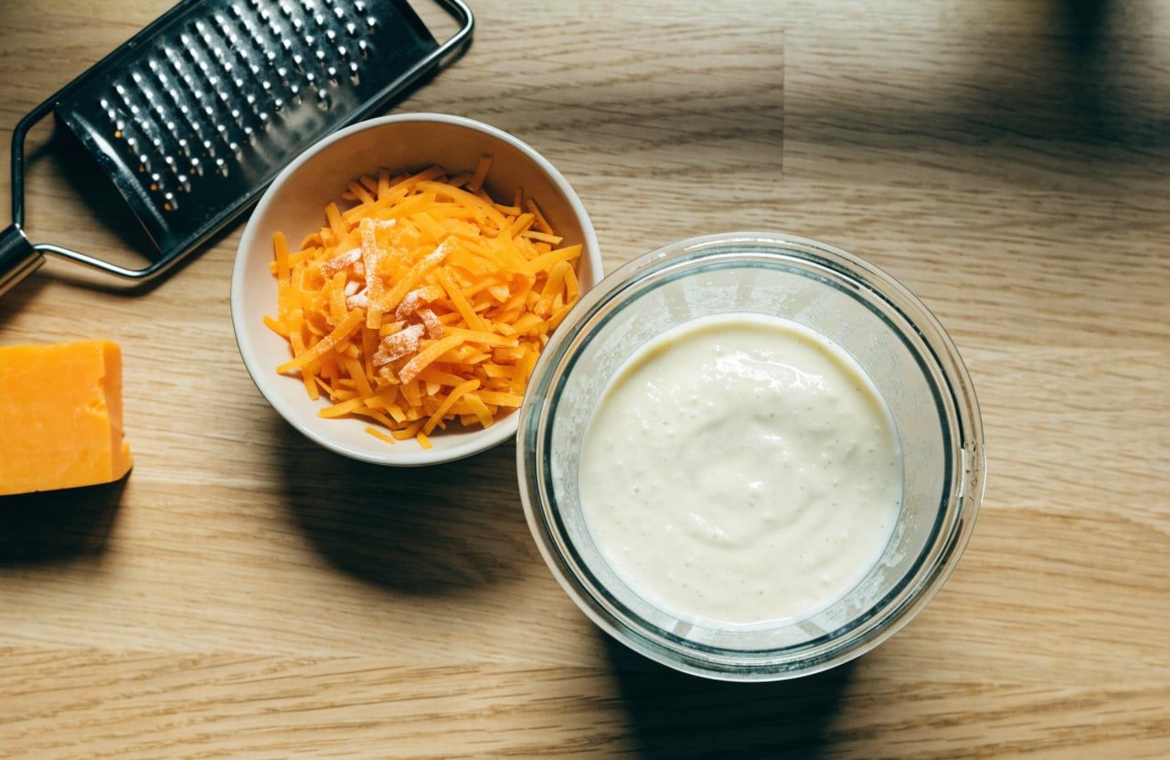 Blender jar of thick smooth cottage cheese base beside a bowl of shredded cheddar dusted with cornstarch