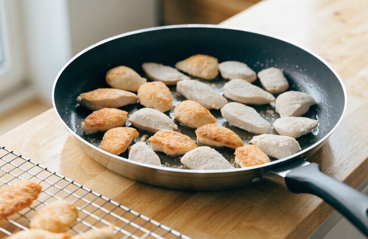 Cornstarch-coated chicken pieces searing golden in a nonstick skillet, spaced apart