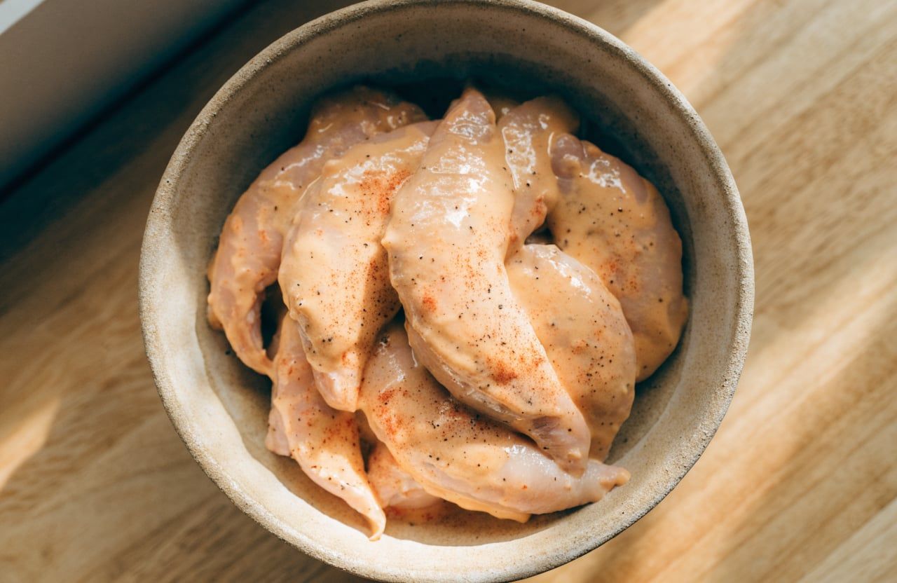 Raw chicken tenders coated in a pale orange Greek yogurt marinade in a bowl