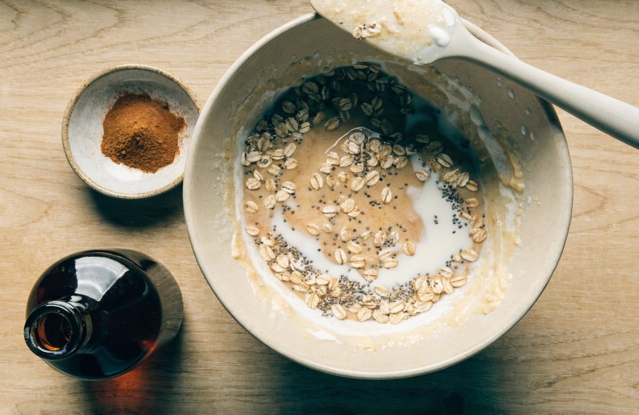 Mixing bowl with loose, glossy Greek yogurt mixture with rolled oats and black chia seeds stirred in