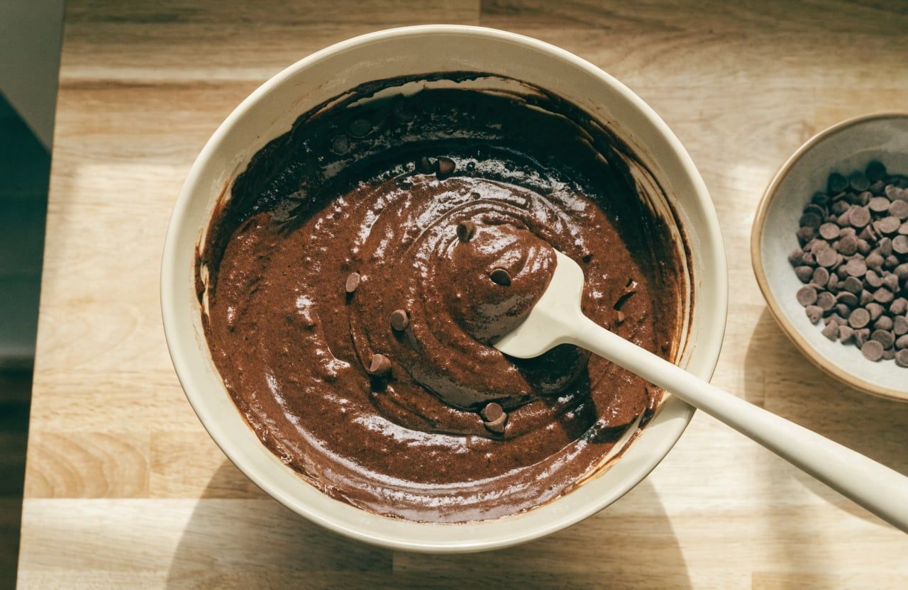 Thick, glossy dark chocolate muffin batter with chocolate chips in a large mixing bowl