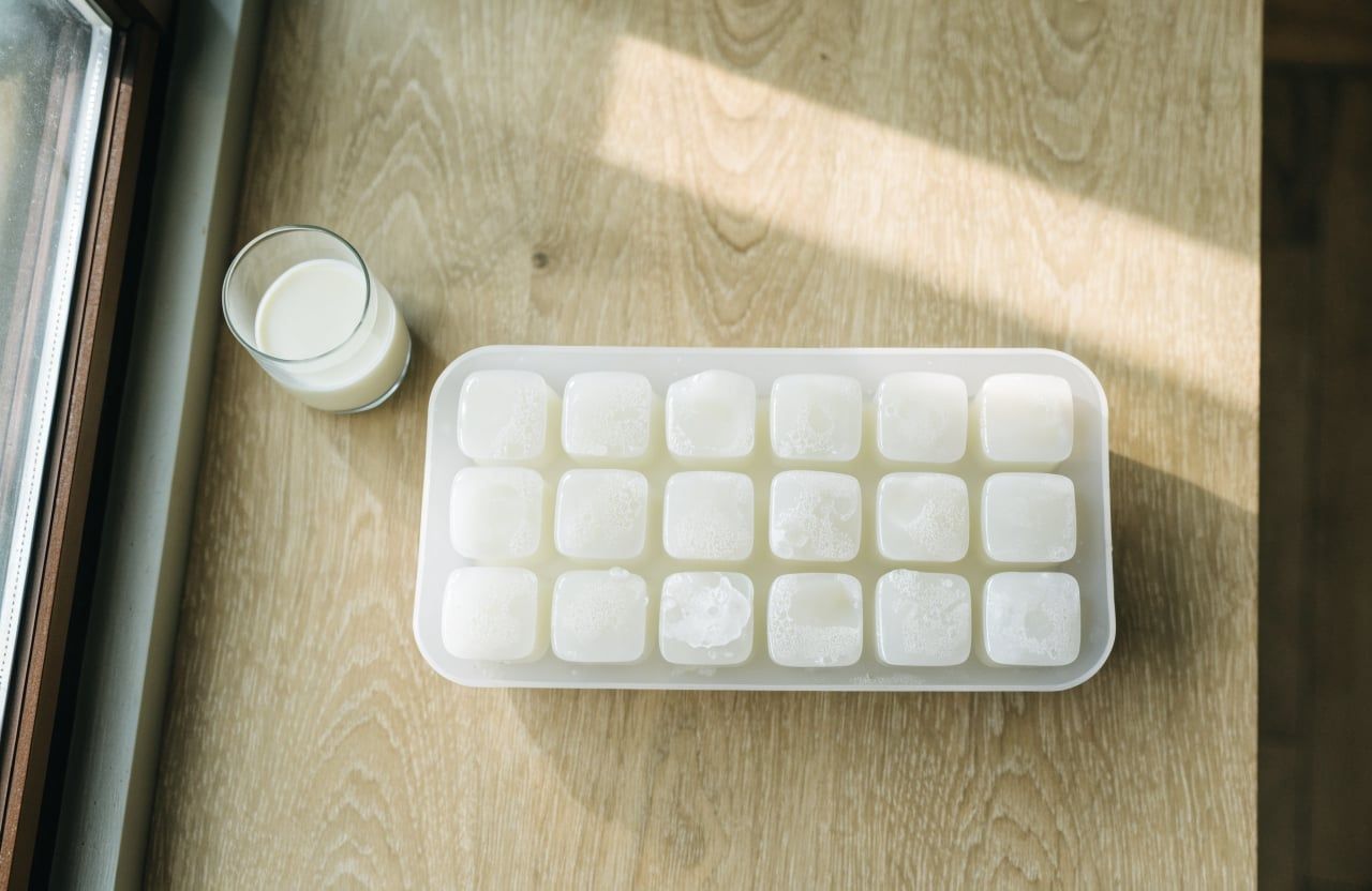 Ice cube tray with opaque white frozen milk cubes on a light oak counter