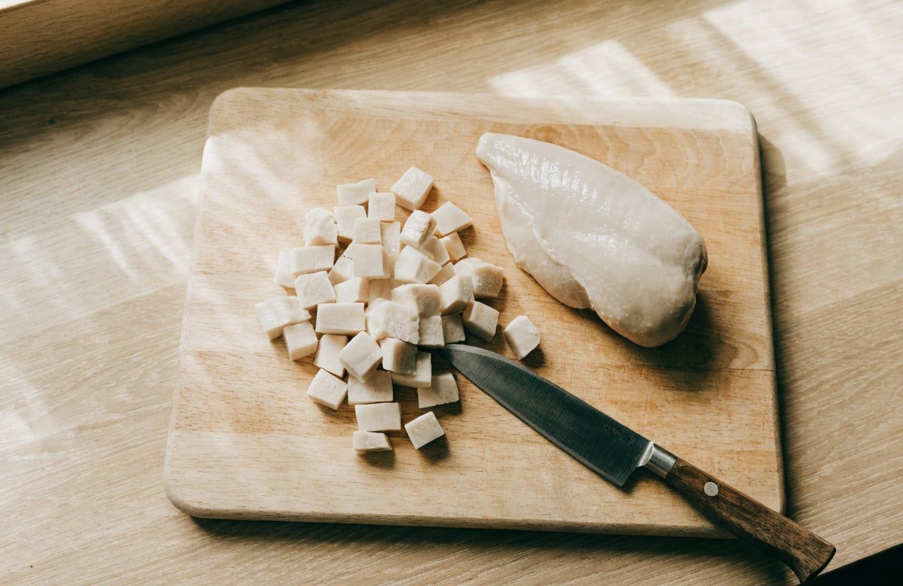 Poached chicken breast diced into white cubes on a wooden cutting board