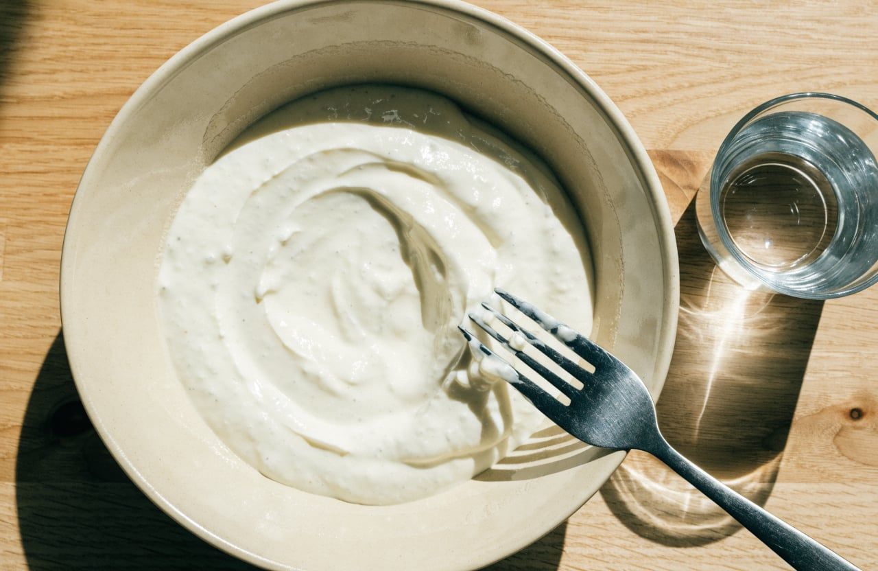 Thick, smooth off-white yogurt with fork tracks in a wide cream bowl