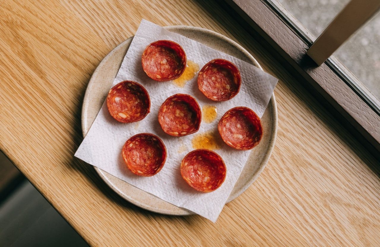 Crisp curled pepperoni slices on a paper towel with orange grease spots on a small plate