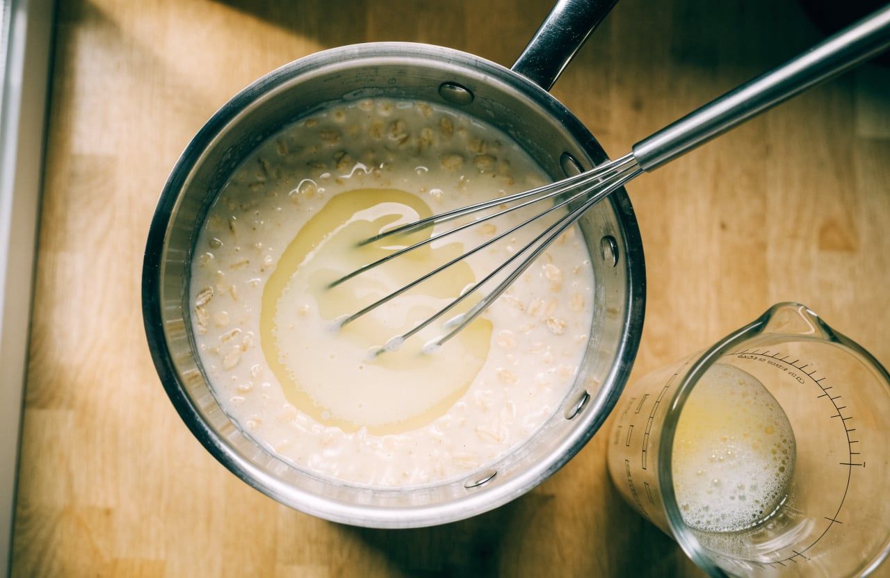 Glossy loose oatmeal with a translucent swirl of egg white and a whisk in the saucepan