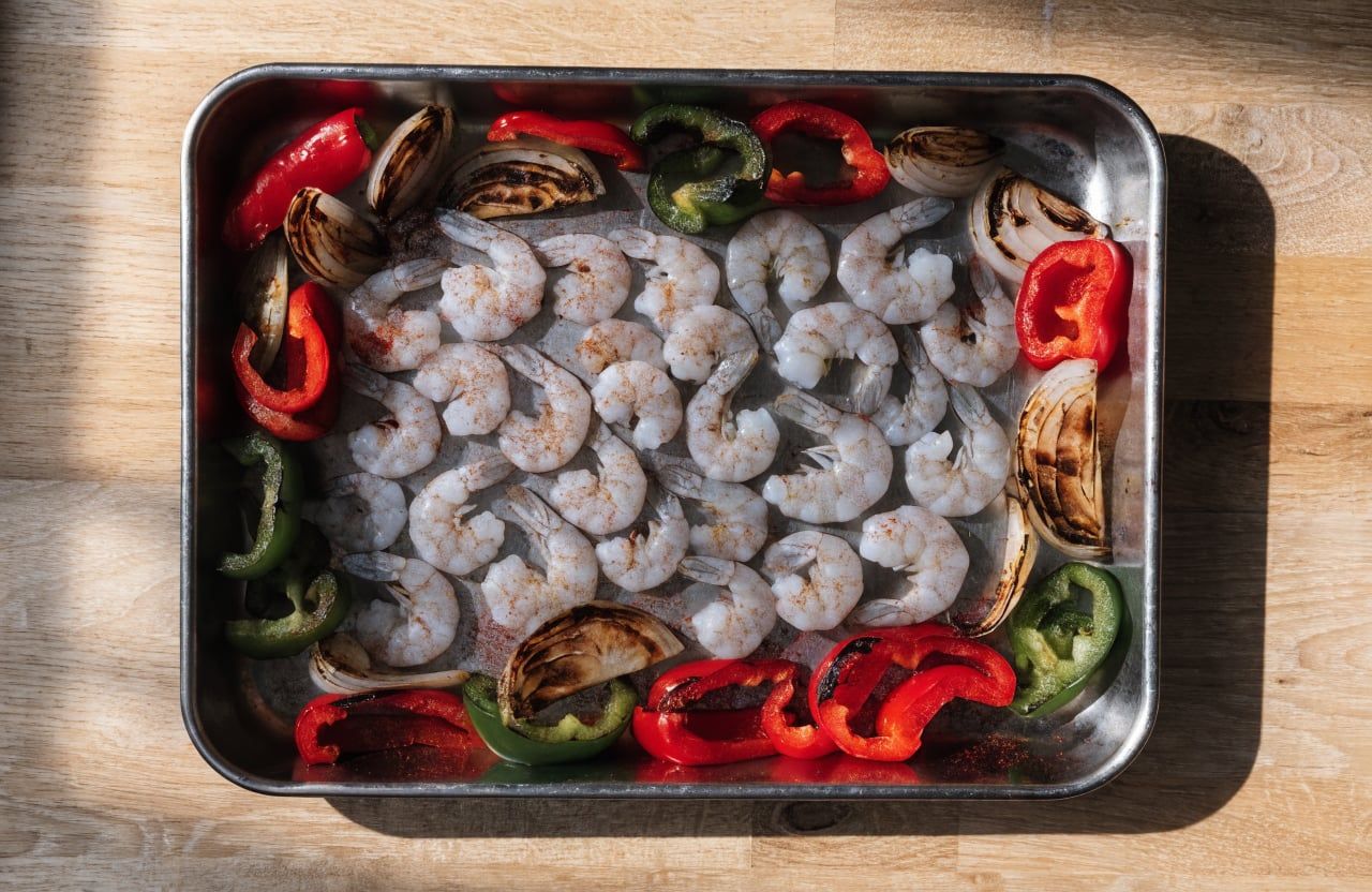 Charred peppers and onions pushed to the edges of a sheet pan with raw seasoned shrimp in the center