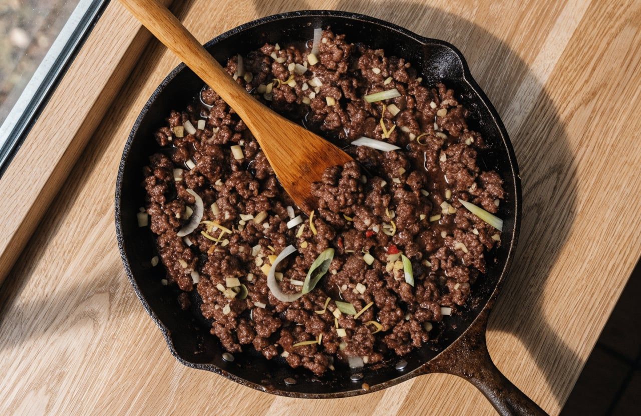 Ground beef crumbles coated in a sticky dark soy glaze with green onion and garlic in a skillet