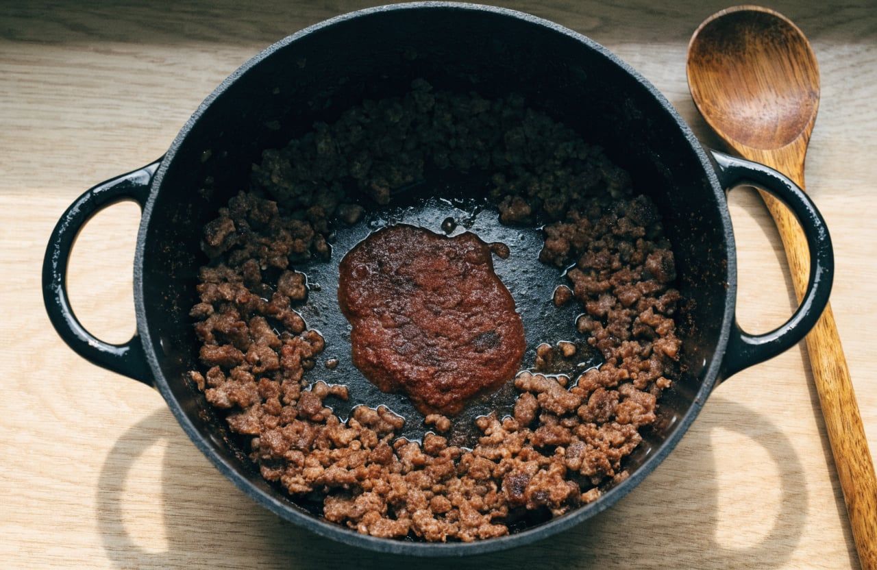 Brick-red toasted tomato paste and chili spices in the center of a pot of browned turkey