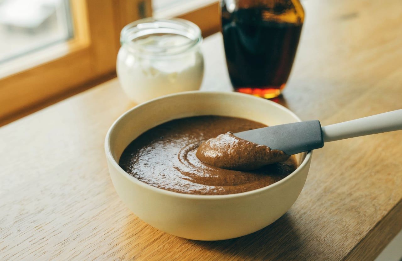 Deep brown brownie batter mixed with Greek yogurt, holding soft ribbons on a spatula
