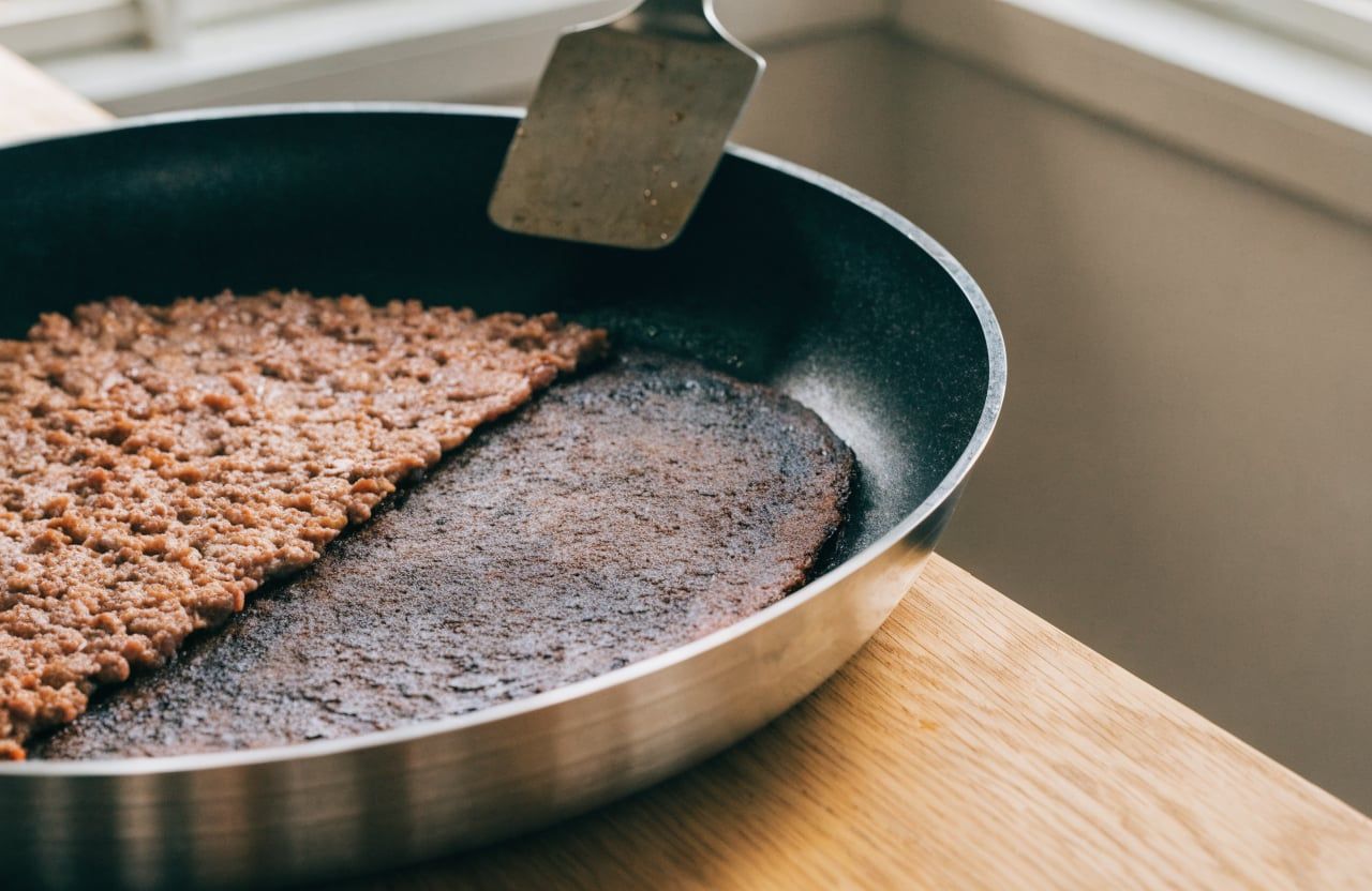 Ground beef seared into a deep brown crust in a skillet, partly flipped