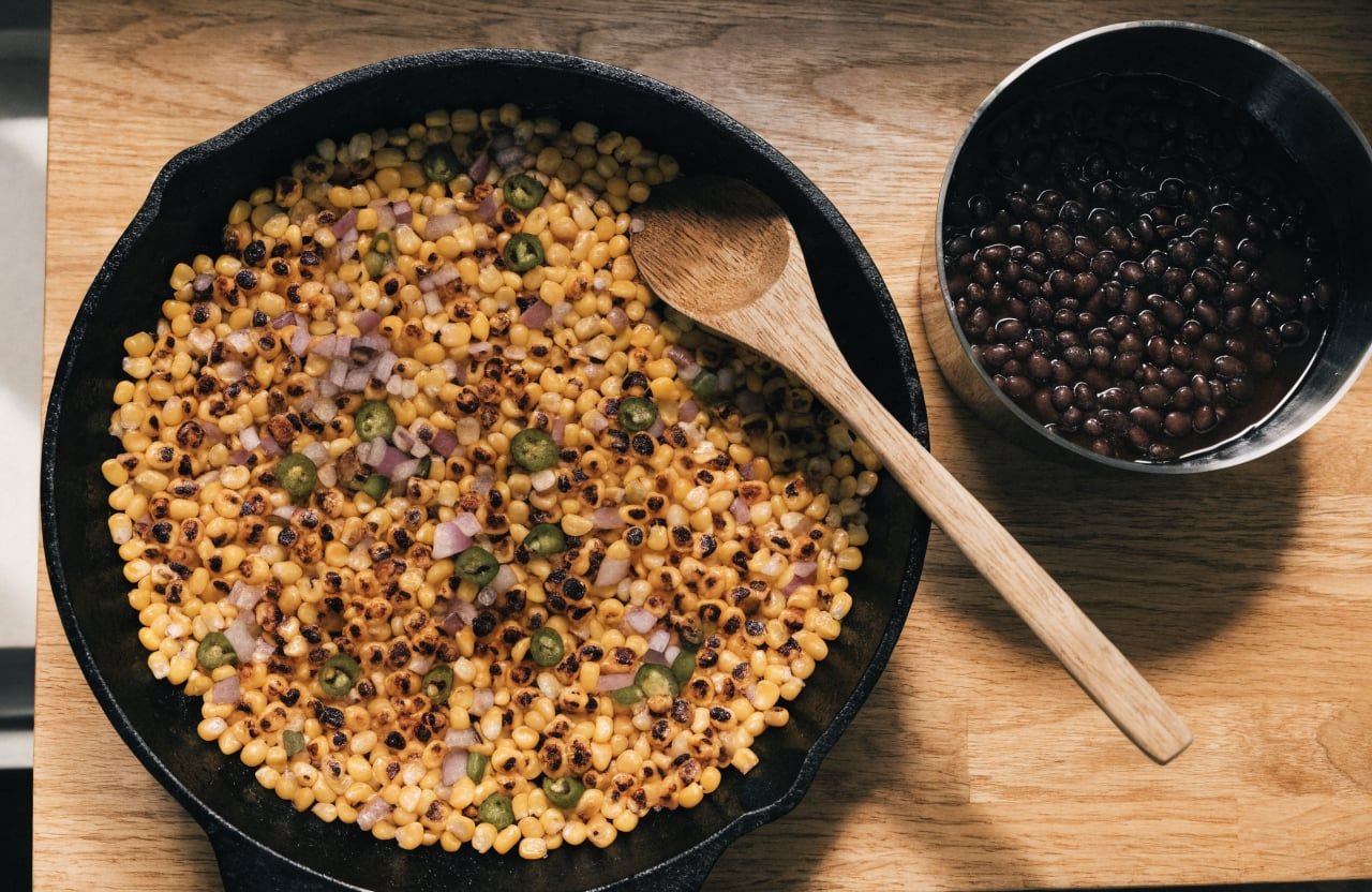 Charred corn kernels with brown spots in a cast-iron skillet with diced red onion and jalapeño
