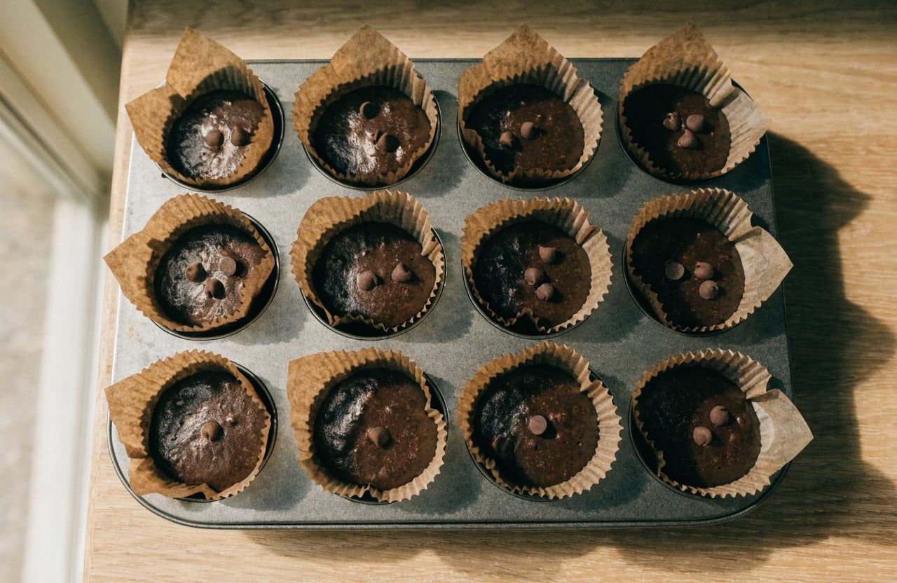 Muffin pan with twelve cups filled to the rim with chocolate batter topped with chocolate chips