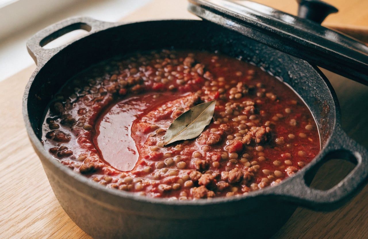 Thick simmering tomato sauce with ground beef and brown lentils in a Dutch oven