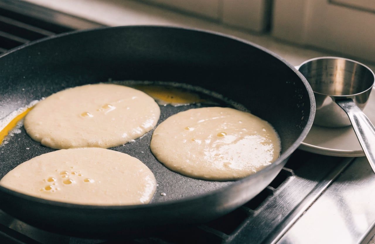 Three rounds of thick pale batter cooking in a nonstick skillet with small bubbles forming