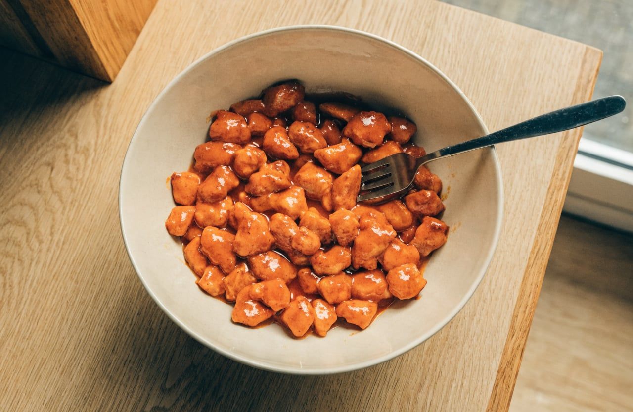 Chopped chicken coated in glossy orange-red buffalo sauce in a large mixing bowl