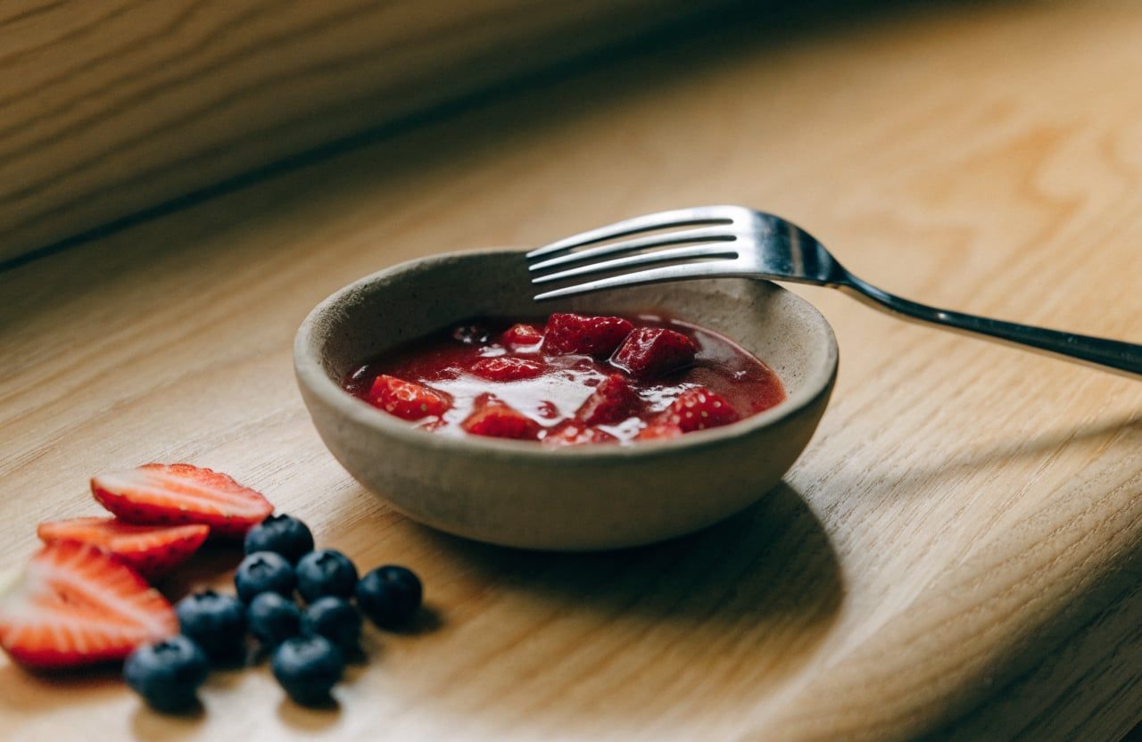 Strawberries mashed with honey into a juicy red sauce in a small bowl
