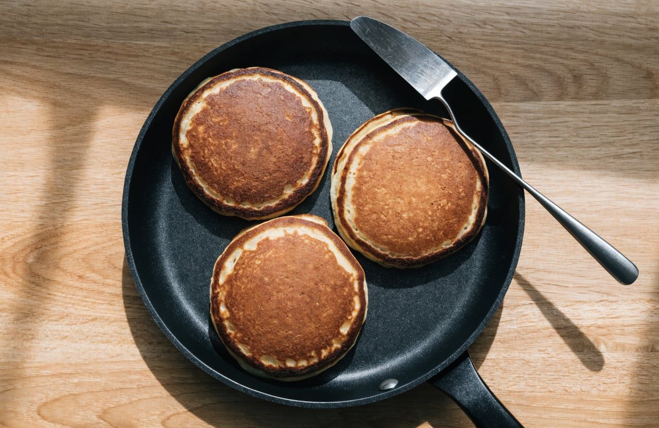Flipped cottage cheese pancakes with deep golden tops cooking in a nonstick skillet