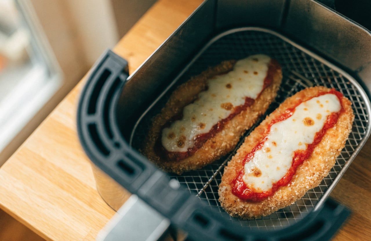 Two chicken cutlets in an air fryer basket topped with marinara and bubbling mozzarella