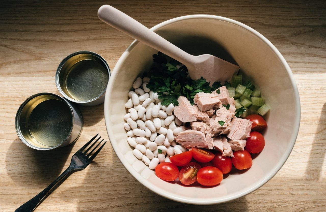Large flakes of tuna folded into white beans, cherry tomatoes, celery and parsley in a mixing bowl