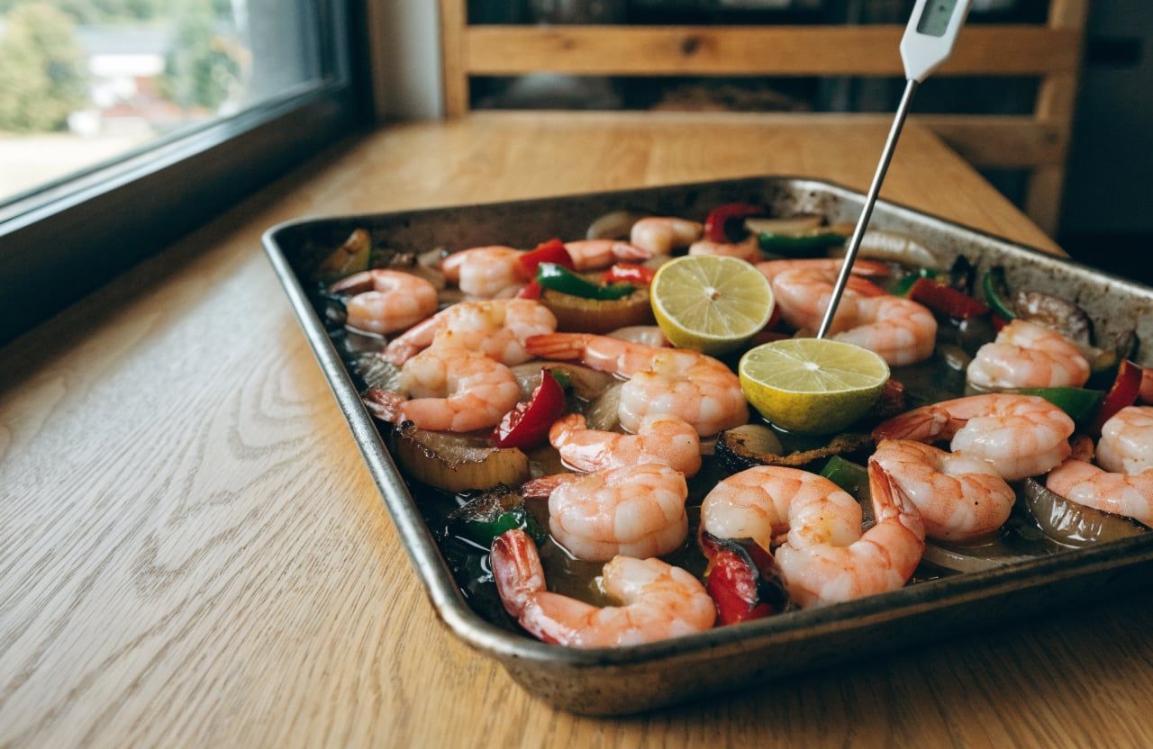 Sheet pan of cooked pink shrimp and charred fajita vegetables with a thermometer in one shrimp