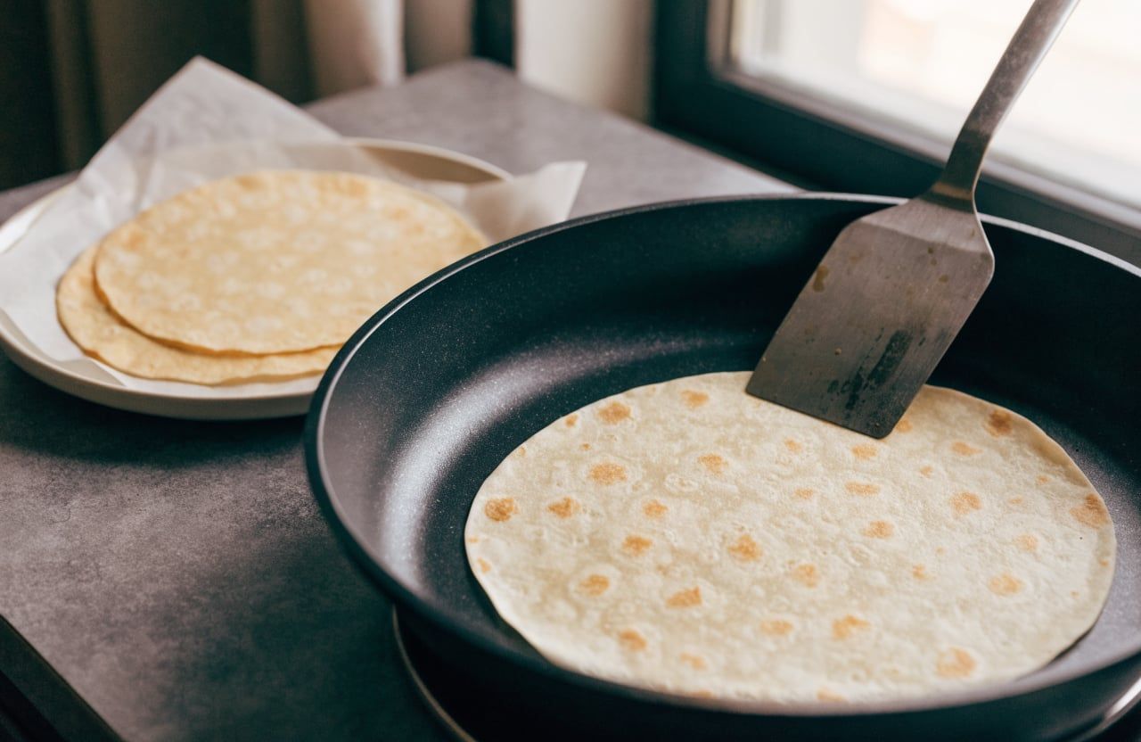 Flipped cottage cheese wrap golden side up in a skillet, finished wraps on parchment beside it