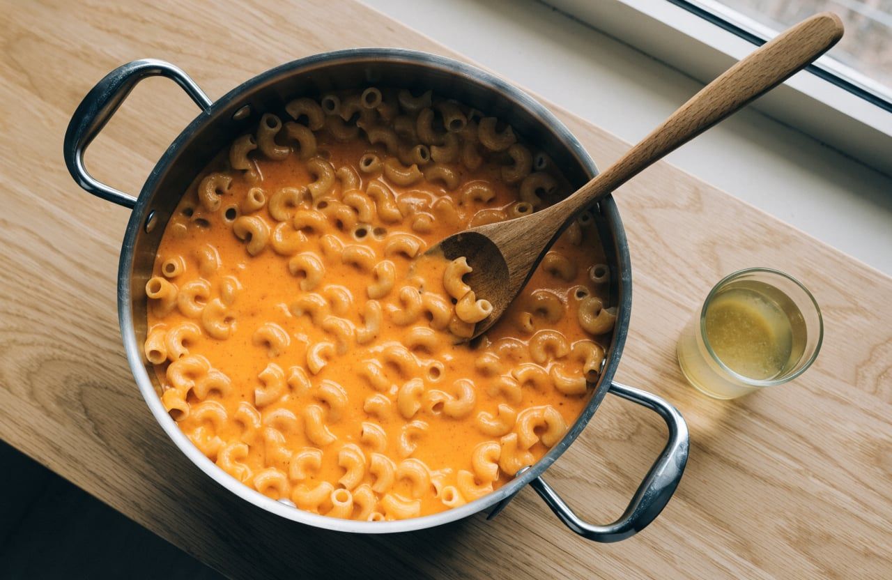 Elbow macaroni folded into creamy orange cheese sauce in a large pot
