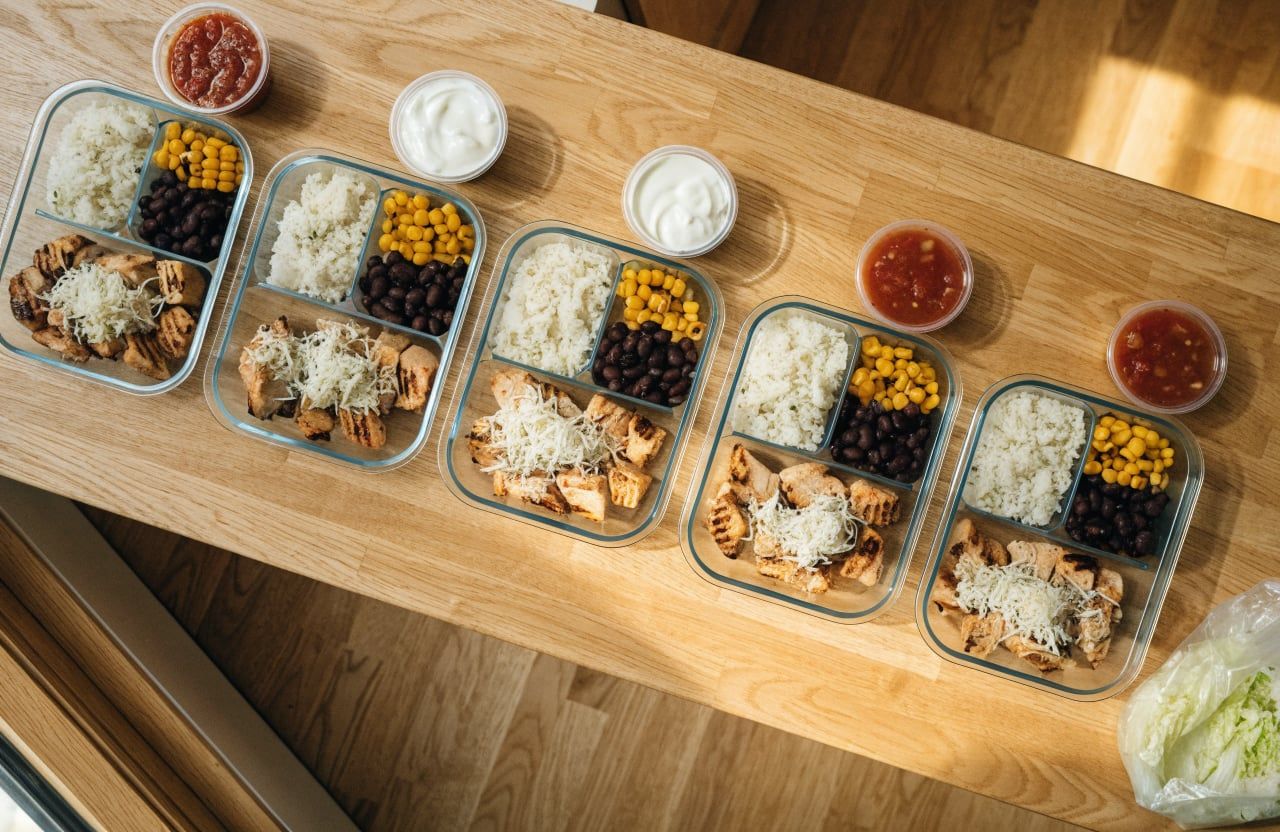 Five meal prep containers with rice, diced chipotle chicken, black beans and charred corn