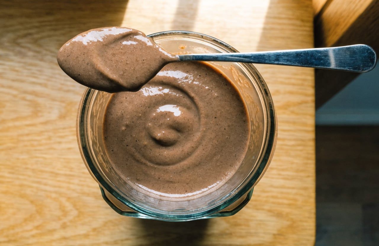 Thick glossy chocolate smoothie in a blender jar with a spoon coated in smoothie