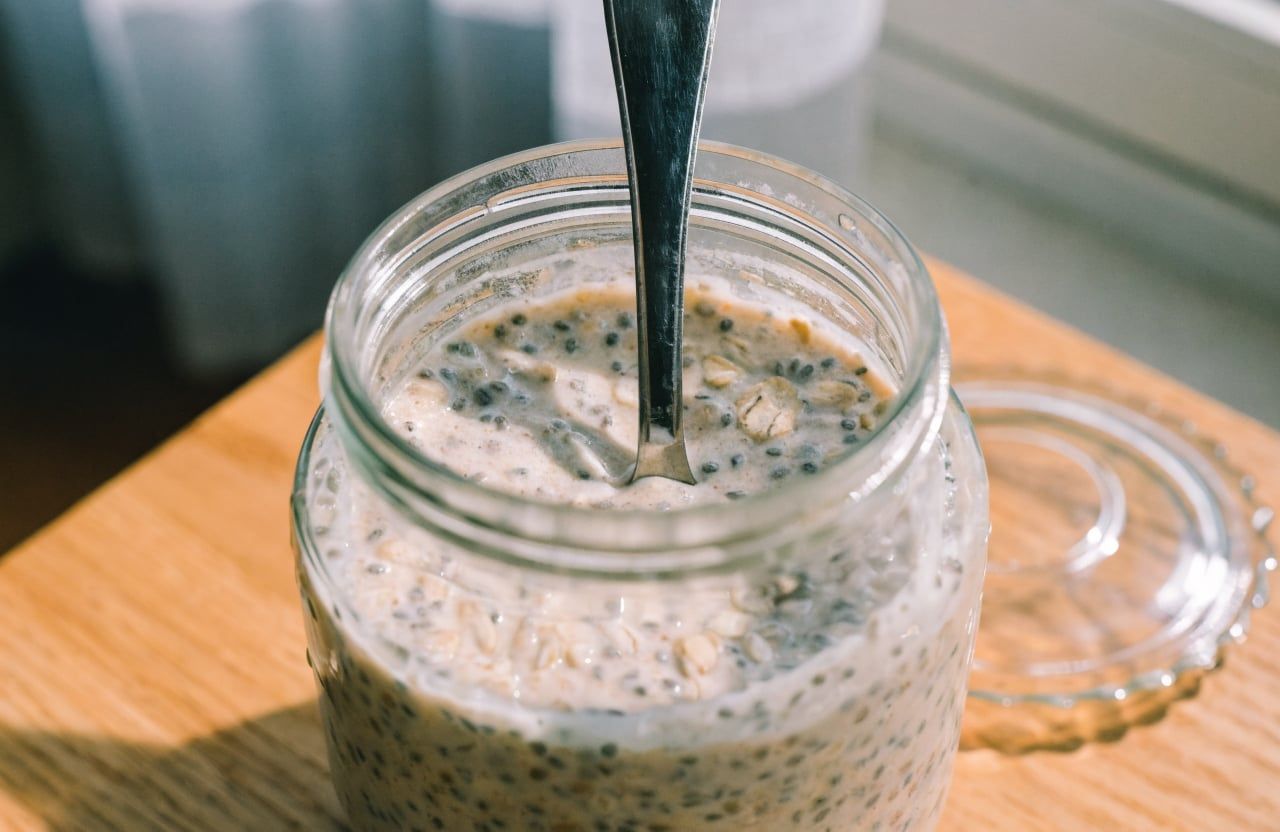 Open jar of chilled overnight oats, thick and set, with a spoon standing upright in the center