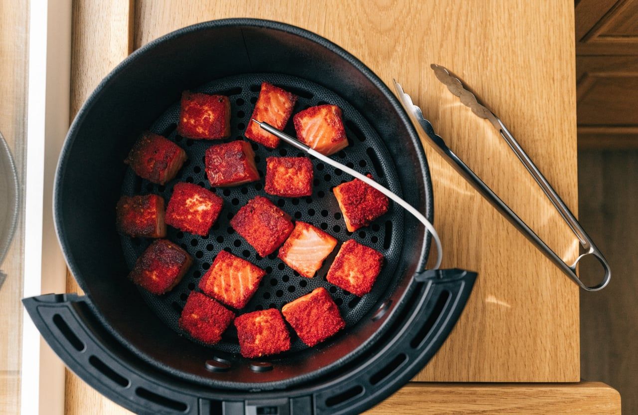 Cooked salmon bites with browned edges spaced out in an air fryer basket