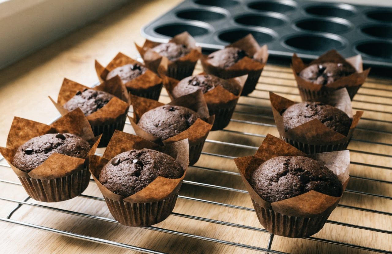 Baked chocolate protein muffins cooling on a wire rack, domed tops with melted chips