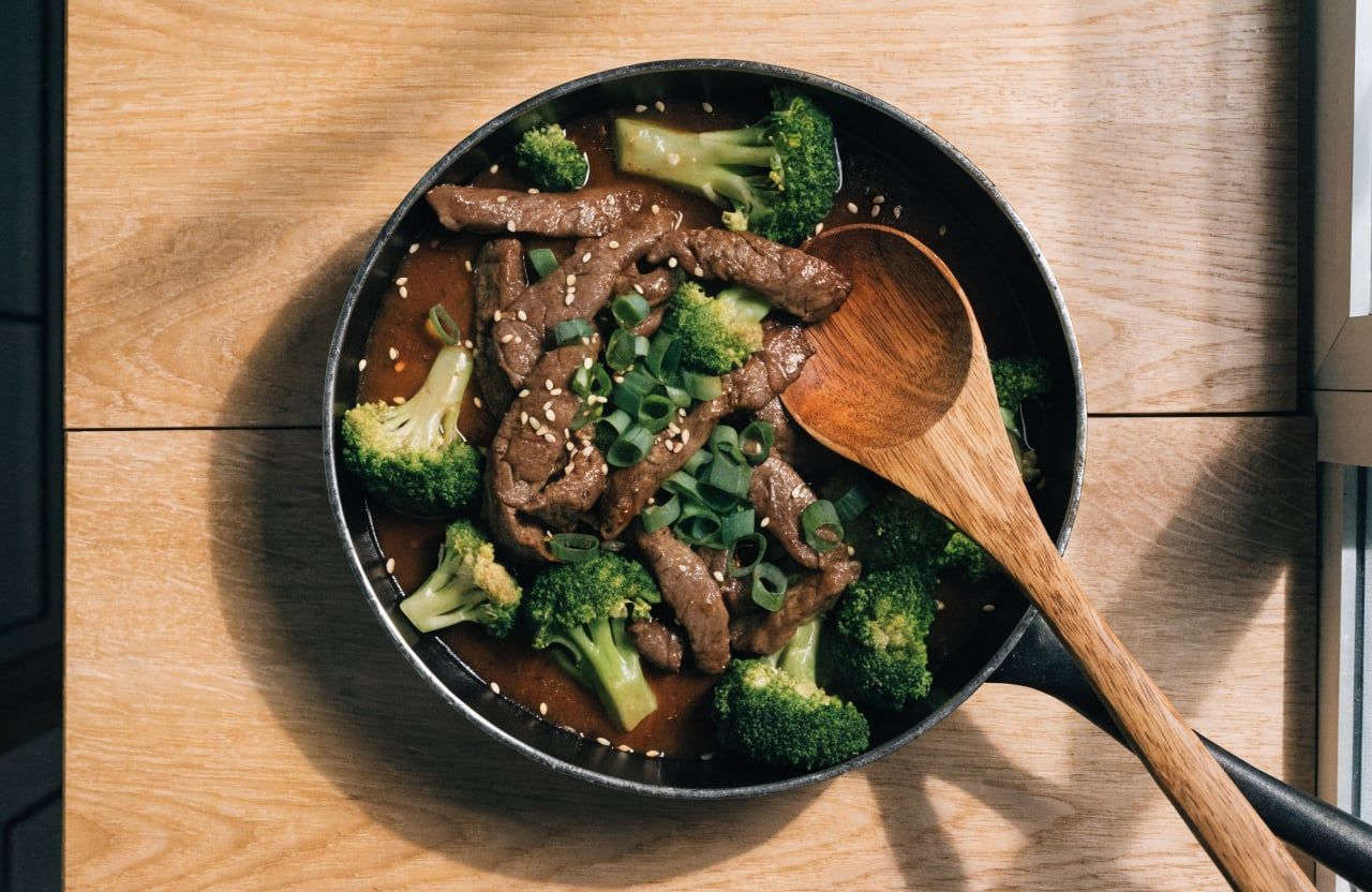 Skillet of beef and broccoli tossed in glossy dark sauce with green onions and sesame