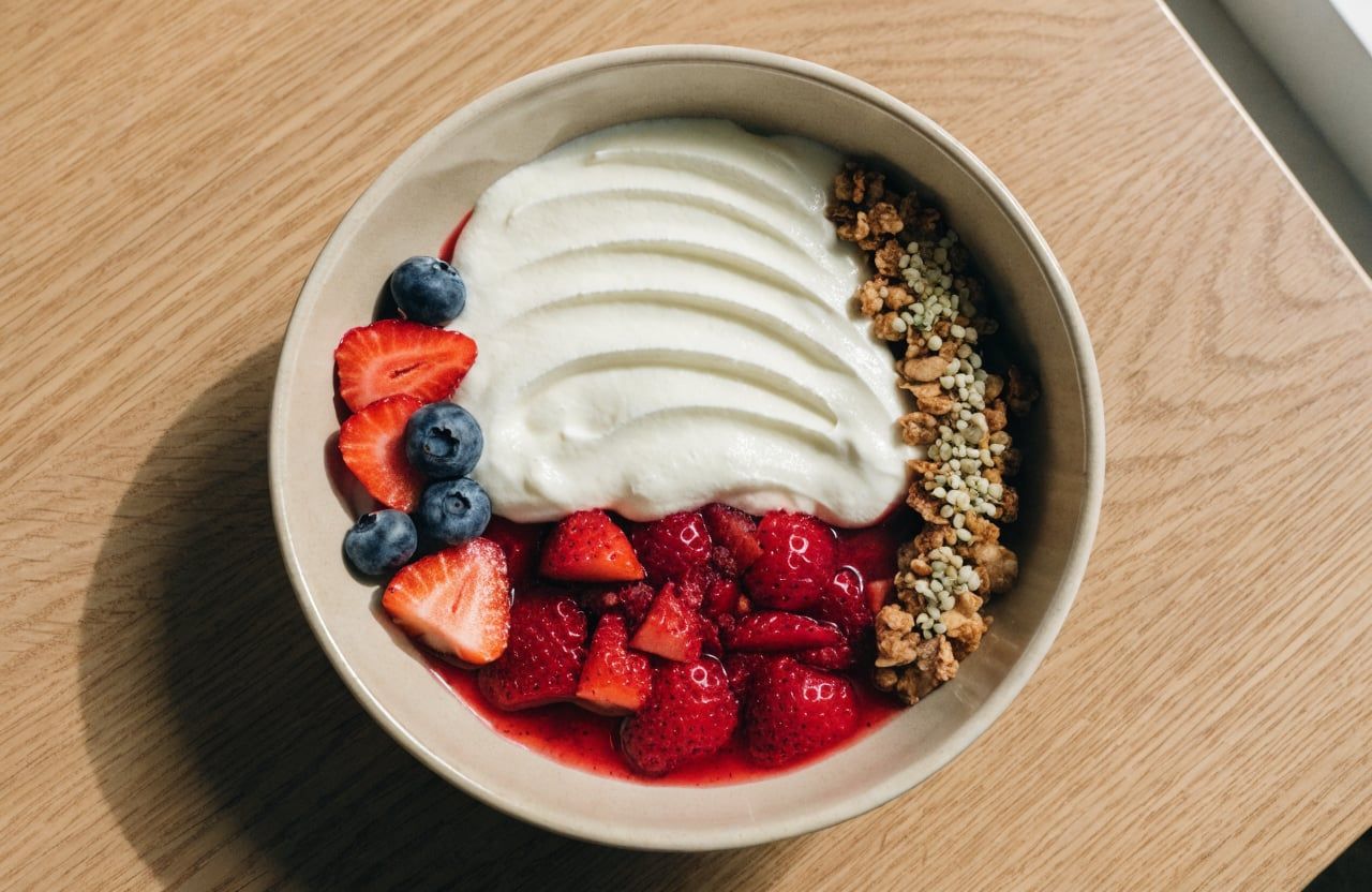 Finished yogurt bowl from above with berry sauce, fresh berries and a strip of granola